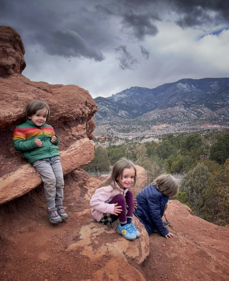 3 kids smiling for a picture on top of a rock formation while hiking.
